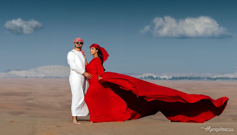 Couple in Dubai desert with flowing red flying dress during a luxury desert photoshoot.
