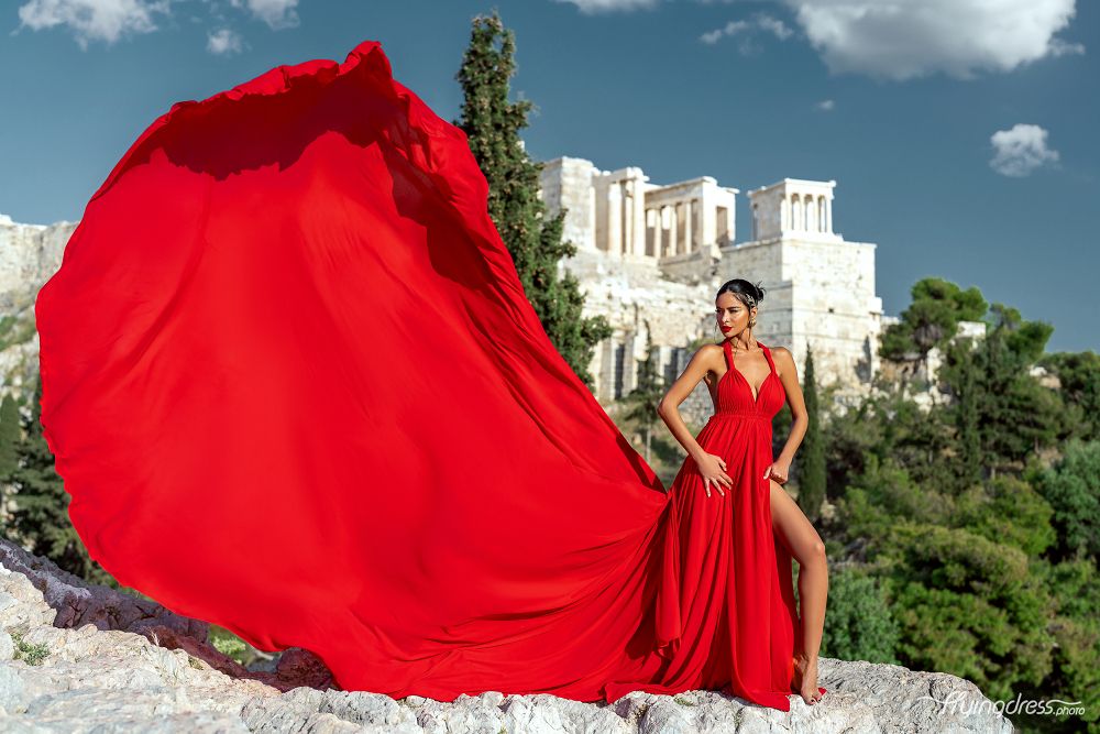 A model captivates against the backdrop of the Acropolis, her silhouette draped in a flowing red dress during a stunning photoshoot in Athens