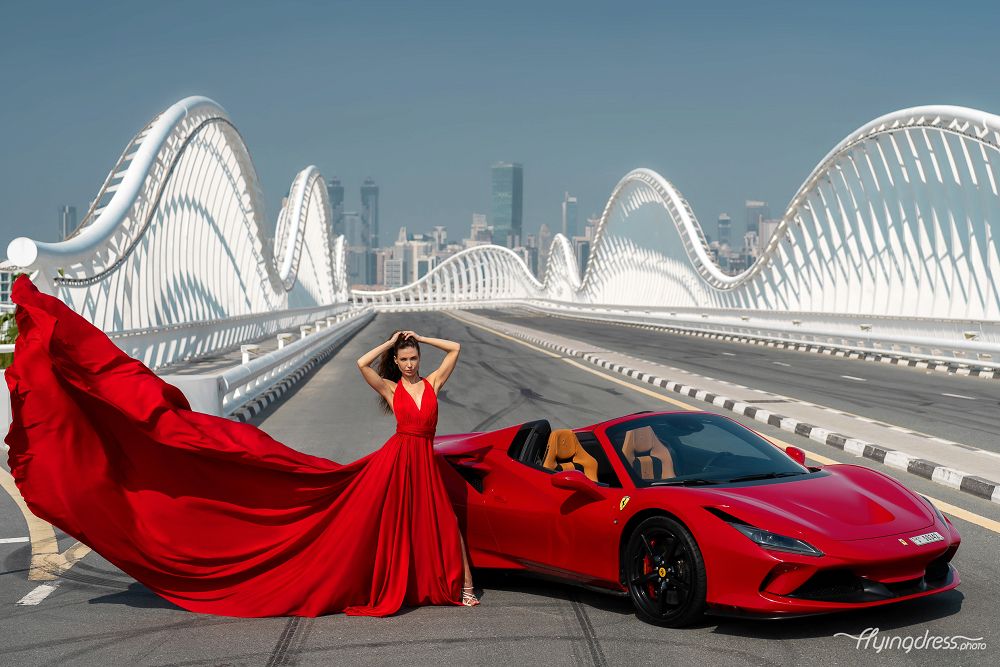 Rev up the glamour! Picture a girl in a striking red dress, poised next to a sleek Ferrari on Dubai's Meydan Bridge.