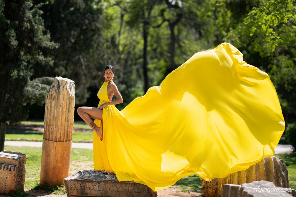 A model poses elegantly amidst Athens' ancient charm, adorned in a luminous yellow flying dress during a captivating photoshoot