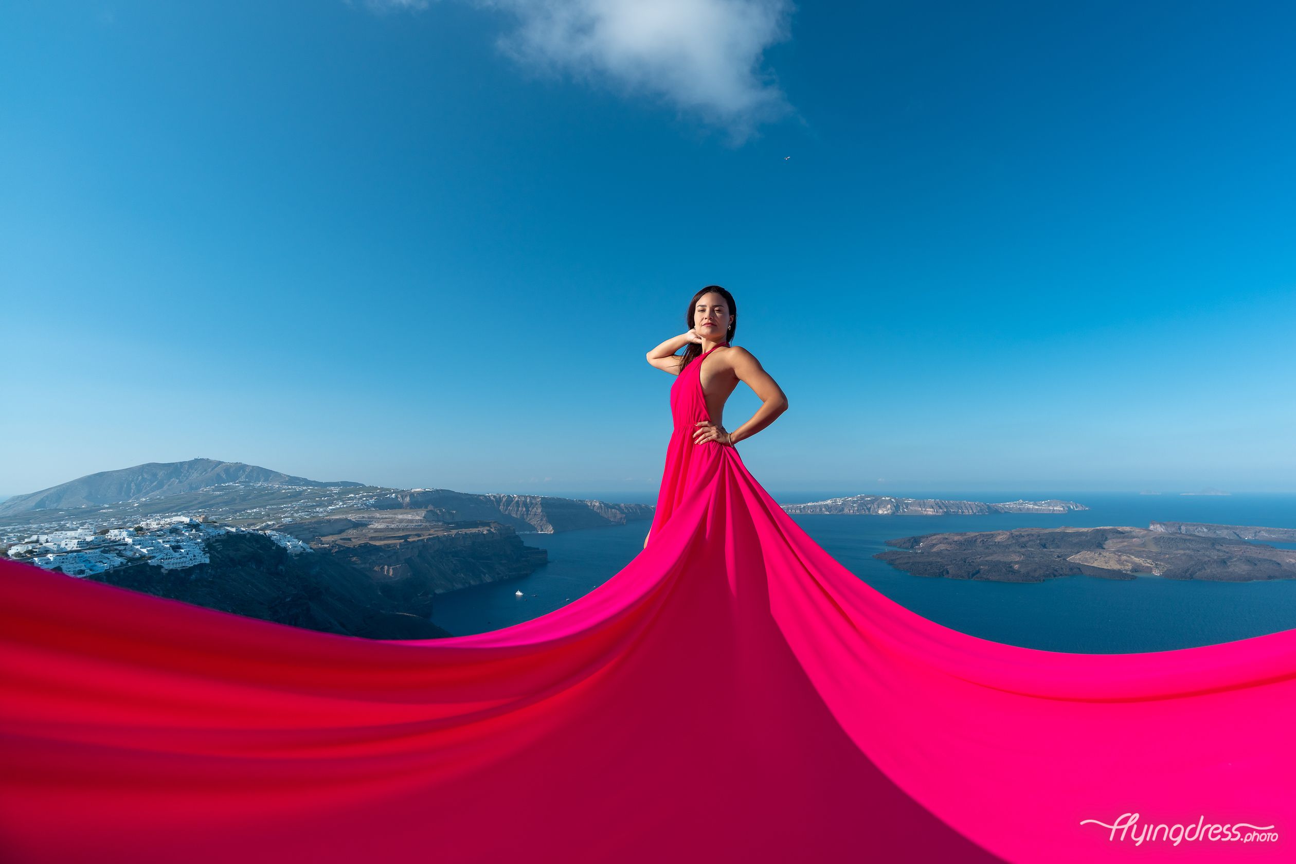 With a fuchsia pink flying dress, the lady enchants Santorini's vistas, her vibrant presence infusing the scene with a touch of whimsy and style.