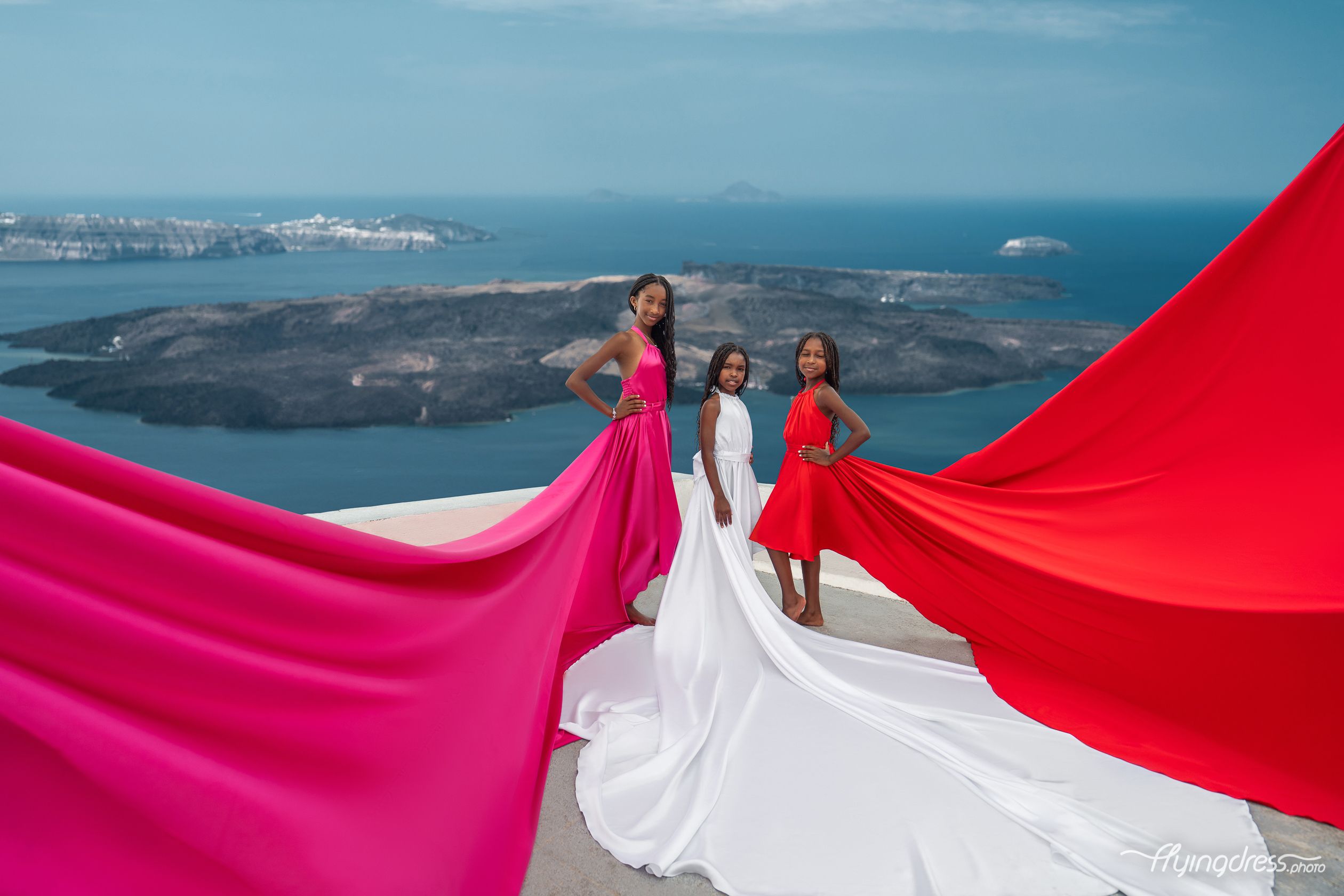 Captivating trio of girls in fuchsia, white, and red flying dresses in Santorini