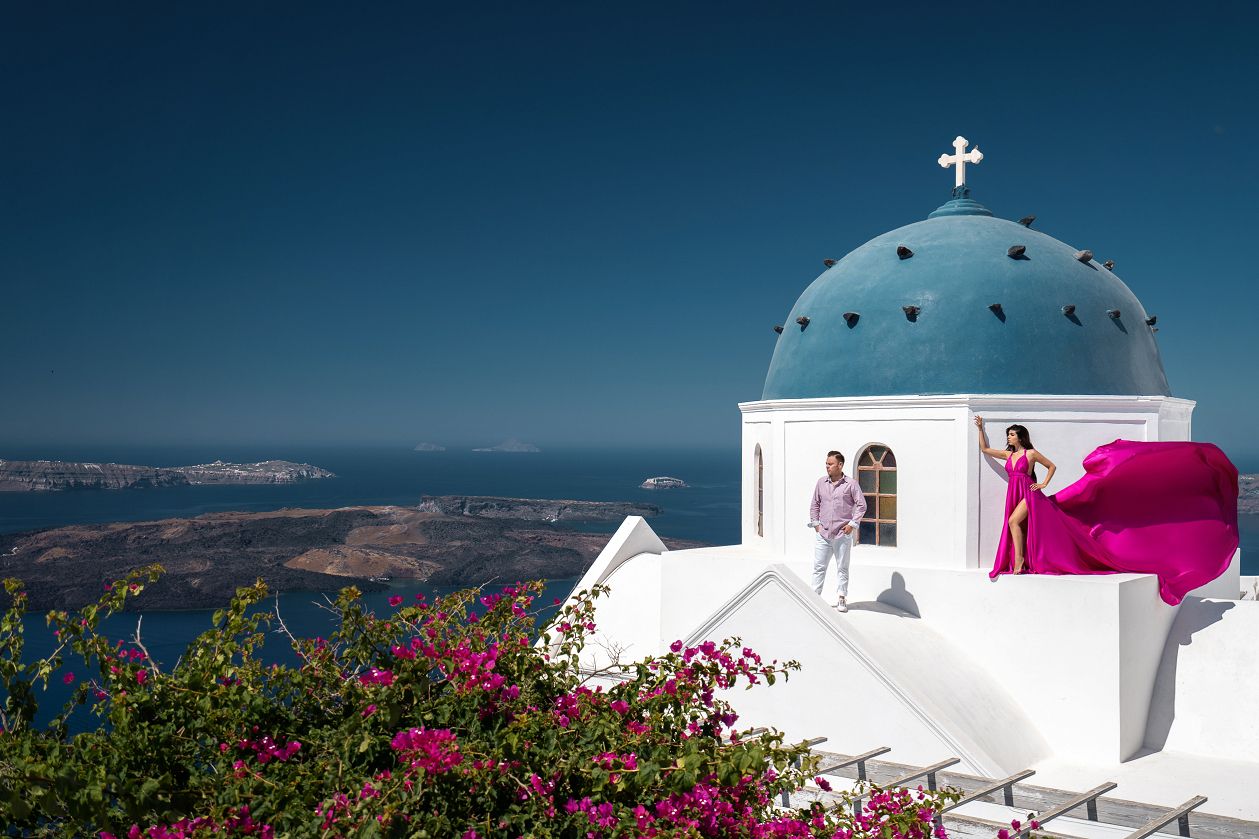 Love story photoshoot in Imerovigli, Greece with a blue dome and volcano view