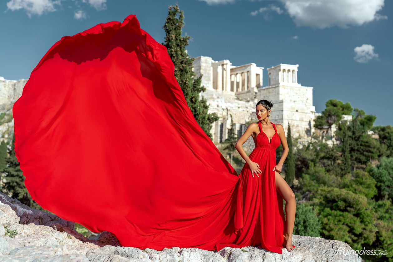 A model captivates against the backdrop of the Acropolis, her silhouette draped in a flowing red dress during a stunning photoshoot in Athens