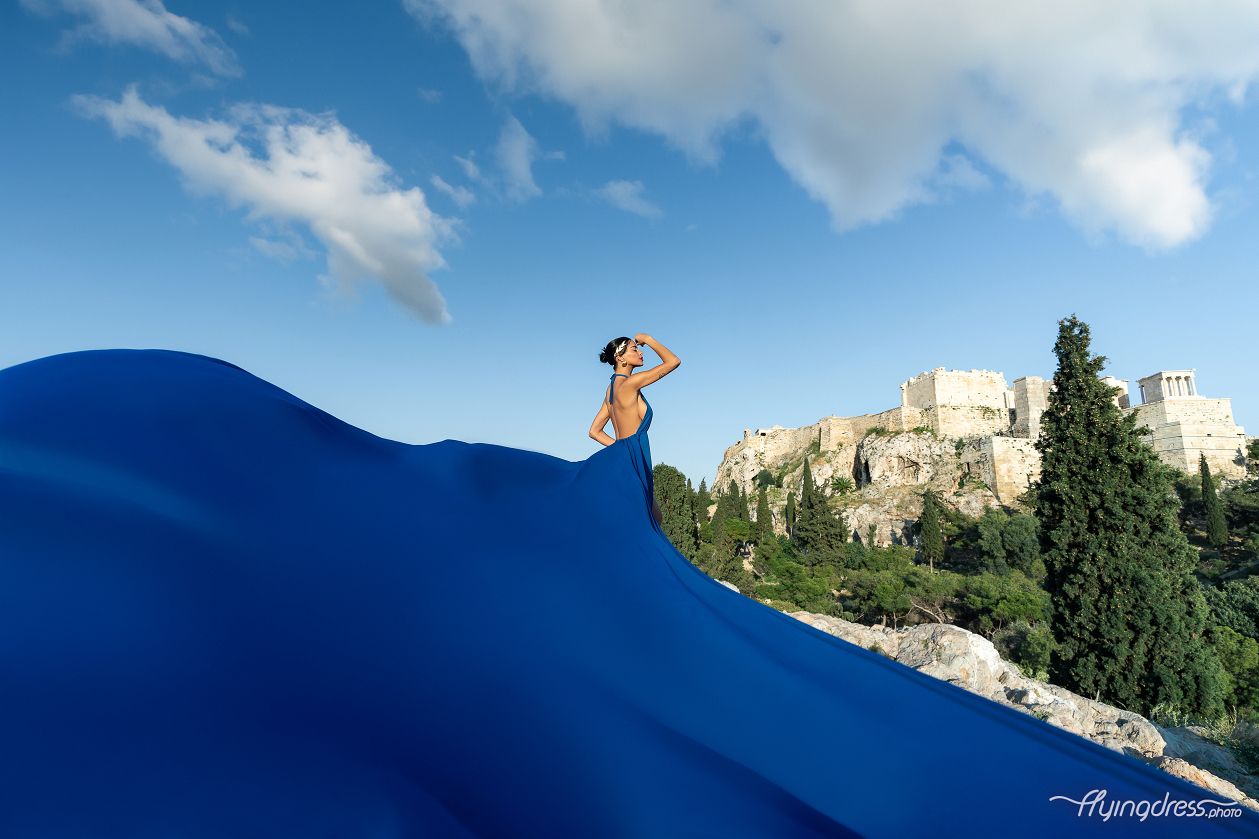 A mesmerizing photoshoot captures a model in a flowing blue dress against the majestic backdrop of the Acropolis in Athens
