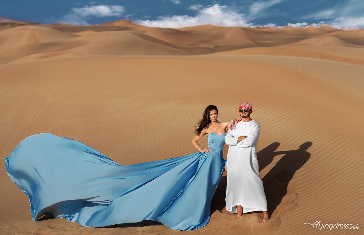 Capturing the essence of romance, a couple takes flight in a dual flying dress photoshoot set against the enchanting backdrop of Dubai's desert