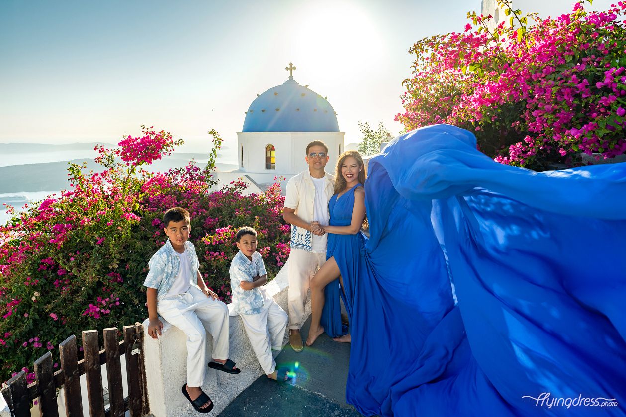 Family photoshoot in Santorini with a captivating caldera and blue dome view. Parents and children are joyfully posing against the iconic white architecture, capturing the essence of a memorable day in this picturesque Greek island paradise.