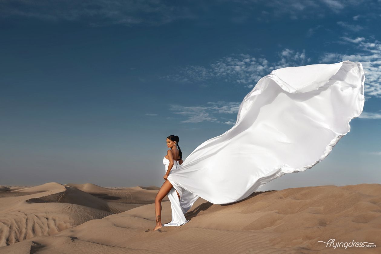 In the captivating expanse of Dubai's desert, a model graces the scene in a mesmerizing flying dress photoshoot, capturing the fusion of elegance and nature against the backdrop of golden sands and boundless horizons.