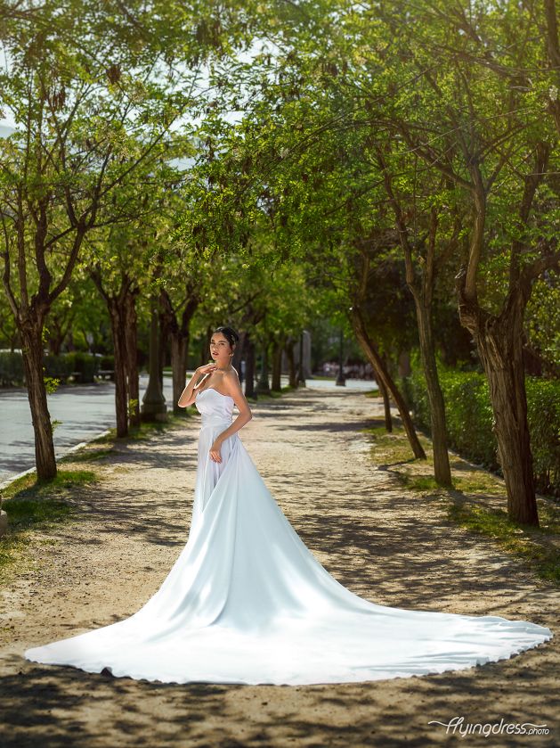 Amidst the verdant oasis of Athens National Garden, a vision of purity emerges as a model dons a flowing white dress, exuding timeless elegance in a captivating photoshoot