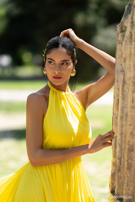 In a serene corner of Athens National Garden, a portrait captures the model's luminous presence, adorned in a striking yellow flying dress, radiating elegance against nature's tranquil canvas