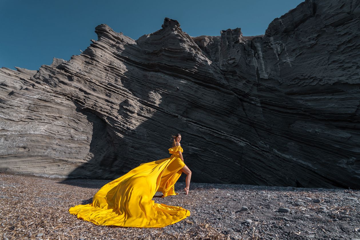 Yellow flying dress shoot at the black beach of Columbus, Santorini
