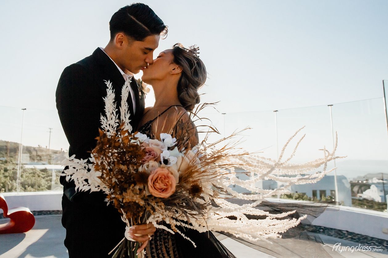 Against the captivating backdrop of Santorini's scenic beauty, an Asian couple, dressed in elegant black attire, embark on a timeless wedding photoshoot, their love and joy radiating through every frame, as they create lasting memories amidst the romantic ambiance of this enchanting Greek island.