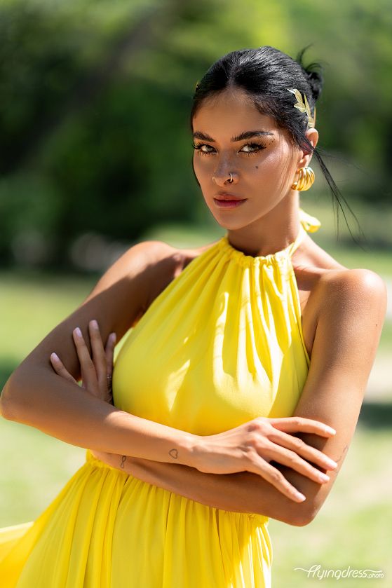 In a captivating portrait, Sara Stamp shines in a radiant yellow dress, her confident demeanor and striking beauty captured with timeless elegance.