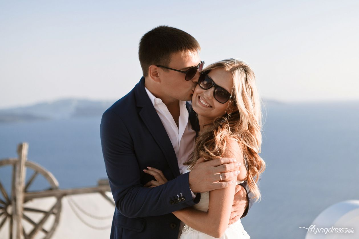 Sharing a sweet kiss on the cheek, a couple in Santorini cherishes a moment of affection, their love manifested through a gentle touch and the warmth of their connection amidst the island's romantic atmosphere.