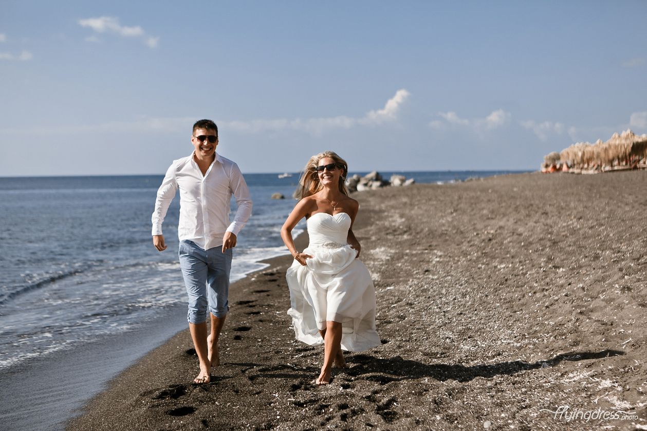 Hand in hand, a couple walks along the black sandy beach of Vlychada in Santorini, their footsteps leaving imprints of love and unity on the volcanic shores, as they embrace the unique beauty of this captivating destination.