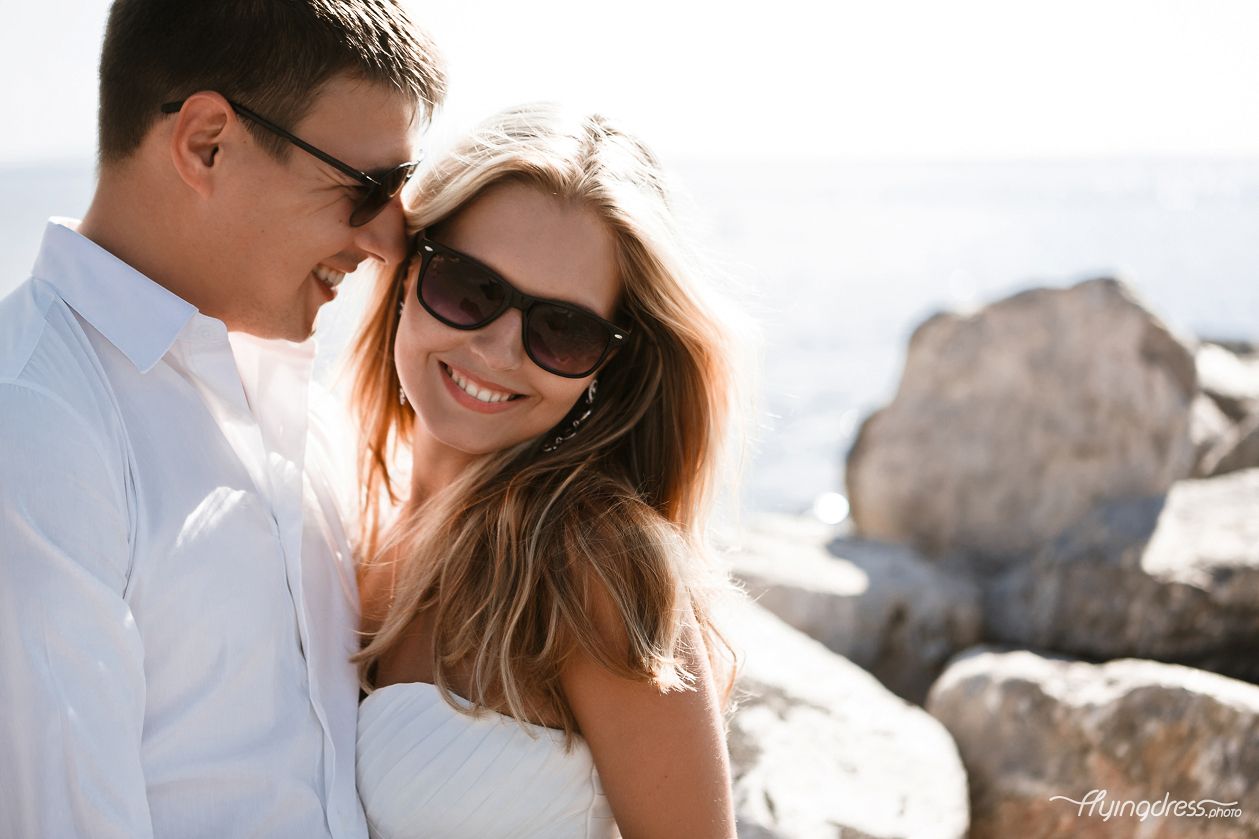 A close portrait of a smiling couple, their eyes locked in affectionate connection, capturing the happiness and love they share while standing on Santorini's black beach.