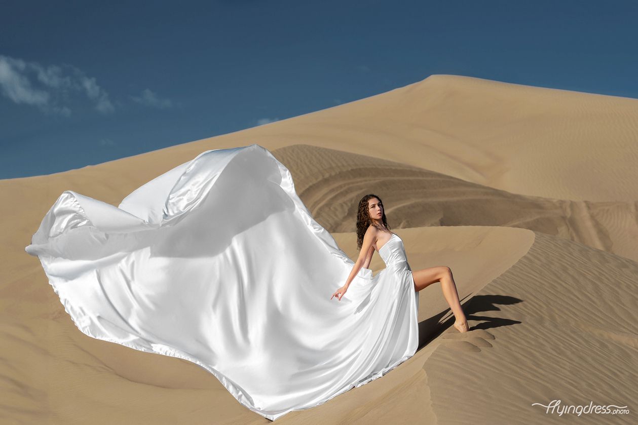 Amidst the serene expanse of Dubai's desert, a girl dances with the wind in a stunning white corset flying dress, embodying elegance against the backdrop of golden sands and boundless horizons in this enchanting photoshoot.