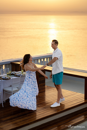 A couple shares a joyful dance on a terrace during a golden sunset, surrounded by an intimate, beautifully set table.