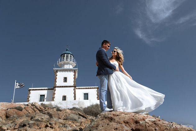 Against the backdrop of Santorini's majestic lighthouse, a wedding couple shares a tender moment, their connection illuminated by the glowing sunset, symbolizing the eternal love and harmony they find in each other's embrace.