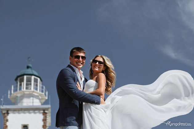Embracing the charm of Santorini's lighthouse, a wedding couple gazes into each other's eyes, their love and devotion creating an enchanting tableau that merges their journey of togetherness with the timeless allure of this iconic island destination.