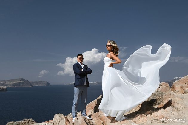 Against the backdrop of Santorini's stunning caldera view, a wedding couple stands at the lighthouse, their love mirroring the grandeur of the volcanic cliffs and the endless expanse of the azure sea, as they embark on a journey of eternal devotion and shared dreams.