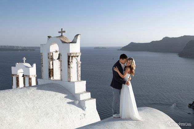 Standing in close proximity to the charming bells, a couple in Santorini captures a moment of closeness and love, their presence intertwined with the timeless traditions and melodies that resonate through the island's enchanting air.