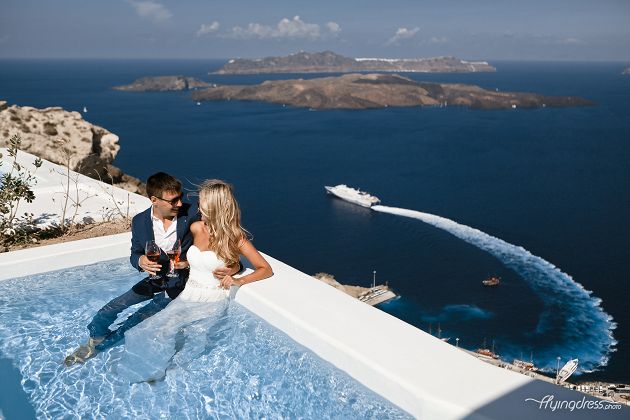 A couple enjoys a blissful moment in the pool, surrounded by the breathtaking caldera view of Santorini, their smiles mirroring the enchanting landscape as they revel in the joy of each other's company.