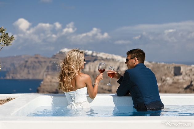 "Alt Text: Floating in the pool, a couple gazes out at the stunning caldera view of Santorini, their eyes captivated by the breathtaking panorama as they immerse themselves in a world of serenity and romance.