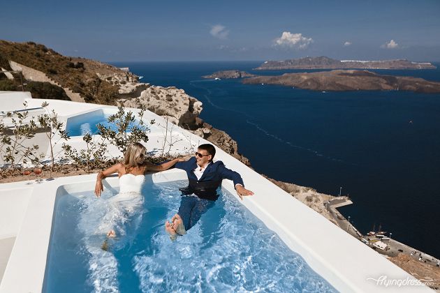 Playfully splashing around in the pool, a couple embraces a carefree spirit as they enjoy moments of fun and laughter, fully embracing the joyous spirit of Santorini's scenic poolside paradise.