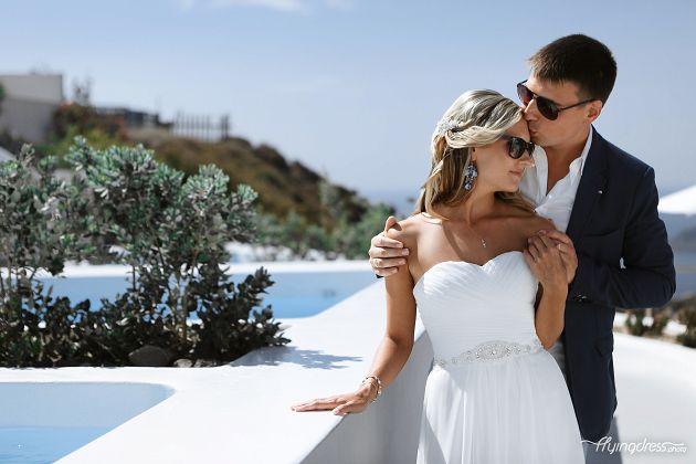 Against the breathtaking backdrop of Santorini's picturesque landscapes, a couple embraces in a tender moment, their love radiating amidst the idyllic beauty of the island, creating a timeless image of romance and enchantment.