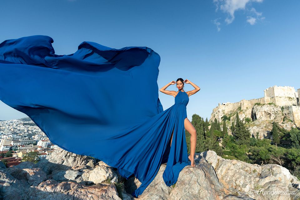 Amidst the timeless allure of Athens, a model shines in a flowing blue dress, her graceful presence harmonizing with the city's historic beauty in a captivating photoshoot