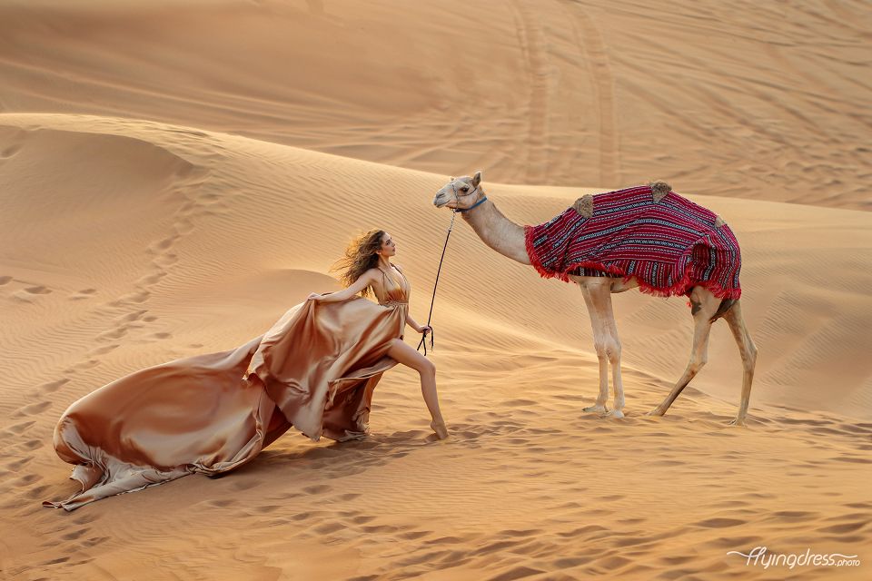 Exquisite desert photoshoot featuring a camel and a golden flying dress, where the majestic dunes become a canvas for the enchanting blend of elegance and desert magic.