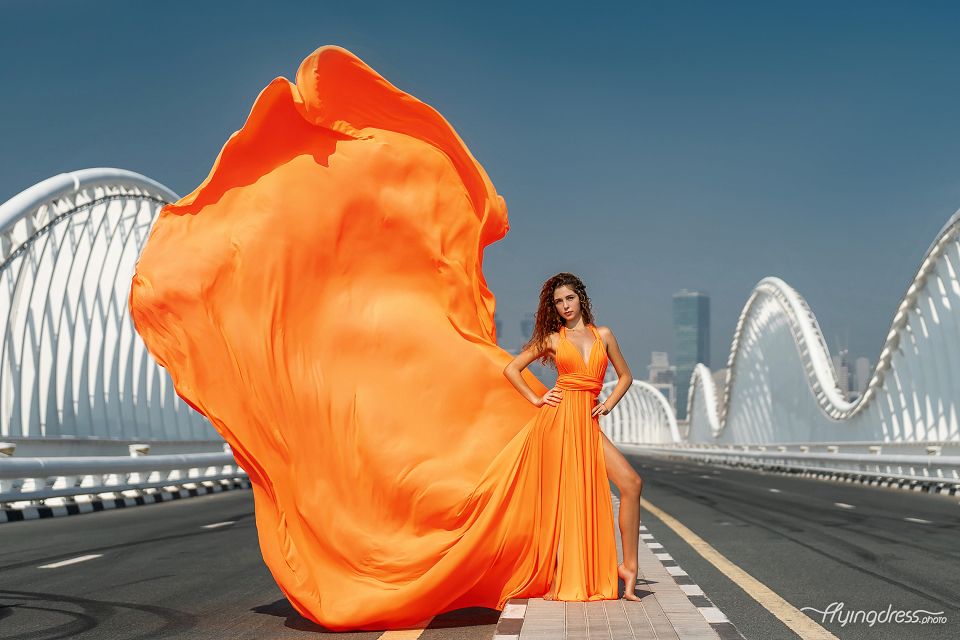 Capture the allure of Dubai's Meydan Bridge as our model graces the scene in a stunning orange flying dress.