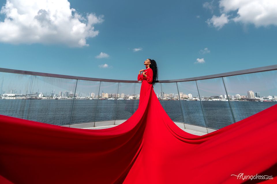 Woman in a red dress leaping with grace at Dubai Creek Harbor, a captivating photoshoot capturing freedom and enchantment by the waterfront.
