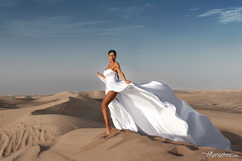 In Dubai's desert, a model enchants in a flying dress photoshoot, where elegance meets nature in the golden embrace of the landscape.