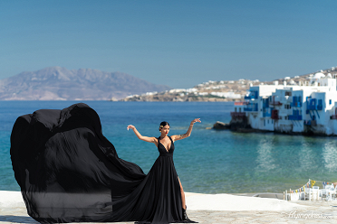 Embrace the elegance of Little Venice in Mykonos with a stunning flying dress photoshoot, where the dramatic black gown contrasts beautifully against the vibrant blue sea and charming waterfront buildings.