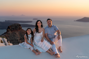 A family enjoys a peaceful moment during sunset in Santorini, with the iconic caldera and islands providing a stunning backdrop.