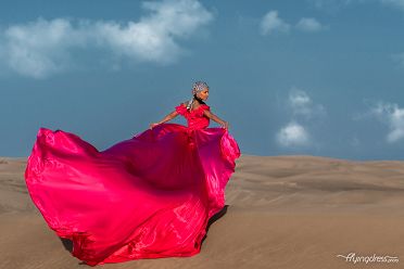 In a stunning display of glamour, models showcase the beauty of a fuchsia satin flying dress, its vibrant hue contrasting against the desert backdrop, creating a captivating and luxurious photoshoot in the heart of Dubai.