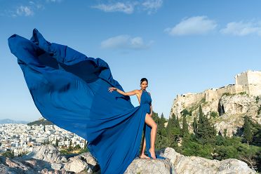 Set against the majestic silhouette of the Acropolis, a model in a flowing blue dress embodies timeless beauty, her presence adding a touch of grace to the iconic Athens skyline in a mesmerizing photoshoot