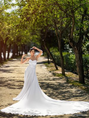 Amidst the lush greenery of Athens National Garden, a model radiates elegance in a white corset flying dress, embodying a vision of timeless beauty in a picturesque photoshoot