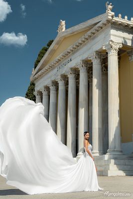 Captivating contrast: a model in a striking red flying dress stands against the majestic Zappeion, creating a mesmerising scene during a photoshoot that blends elegance and historic charm.