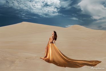 In the golden embrace of Dubai's desert, a vision unfolds as a girl gracefully soars in a captivating gold flying dress, capturing the essence of elegance against the breathtaking backdrop of endless dunes.