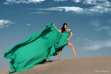 In a breathtaking fusion of elegance and nature, a model graces the scene in a flowing green flying dress, creating a mesmerizing visual symphony against the stunning backdrop of Dubai's desert landscape.