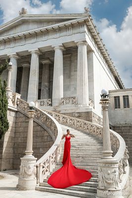 In the grandeur of Vallianeio Megaron, a model in a bold red dress commands attention, epitomizing sophistication and allure in a captivating photoshoot against Athens' historic backdrop