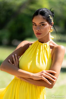 In a captivating portrait, Sara Stamp shines in a radiant yellow dress, her confident demeanor and striking beauty captured with timeless elegance.