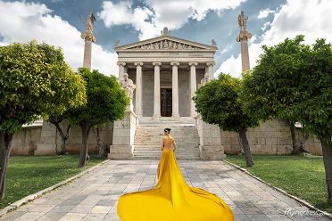 Aglow in a resplendent gold dress, a model dazzles against the backdrop of Athens' historic charm, embodying opulence and sophistication in a mesmerizing photoshoot
